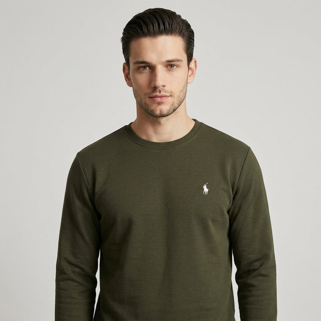 A man wearing an olive green long-sleeve crewneck sweatshirt with the white embroidered Polo Ralph Lauren pony logo on the left chest, paired with blue jeans against a plain white studio background.