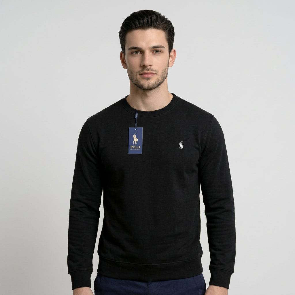 A man wearing a black long-sleeve crewneck sweatshirt with a blue Polo Ralph Lauren hangtag on the chest and a small white polo player logo on the left chest, set against a plain light gray background.