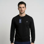 A man wearing a black long-sleeve crewneck sweatshirt with a blue Polo Ralph Lauren hangtag on the chest and a small white polo player logo on the left chest, set against a plain light gray background.